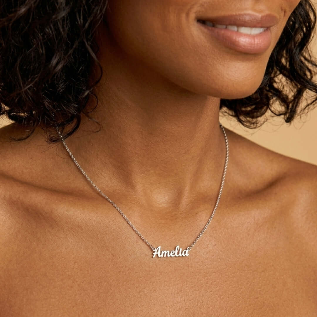 Signature Name Necklace worn by a woman, featuring a personalized silver nameplate with the name 'Amelia'.